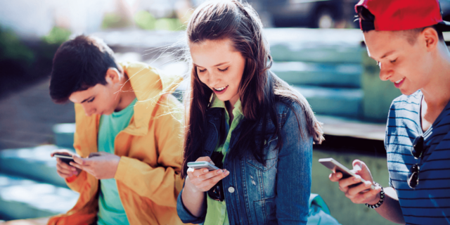 Ein lächelndes Teenager-Mädchen betrachtet seinen Smartphone-BIldschirm